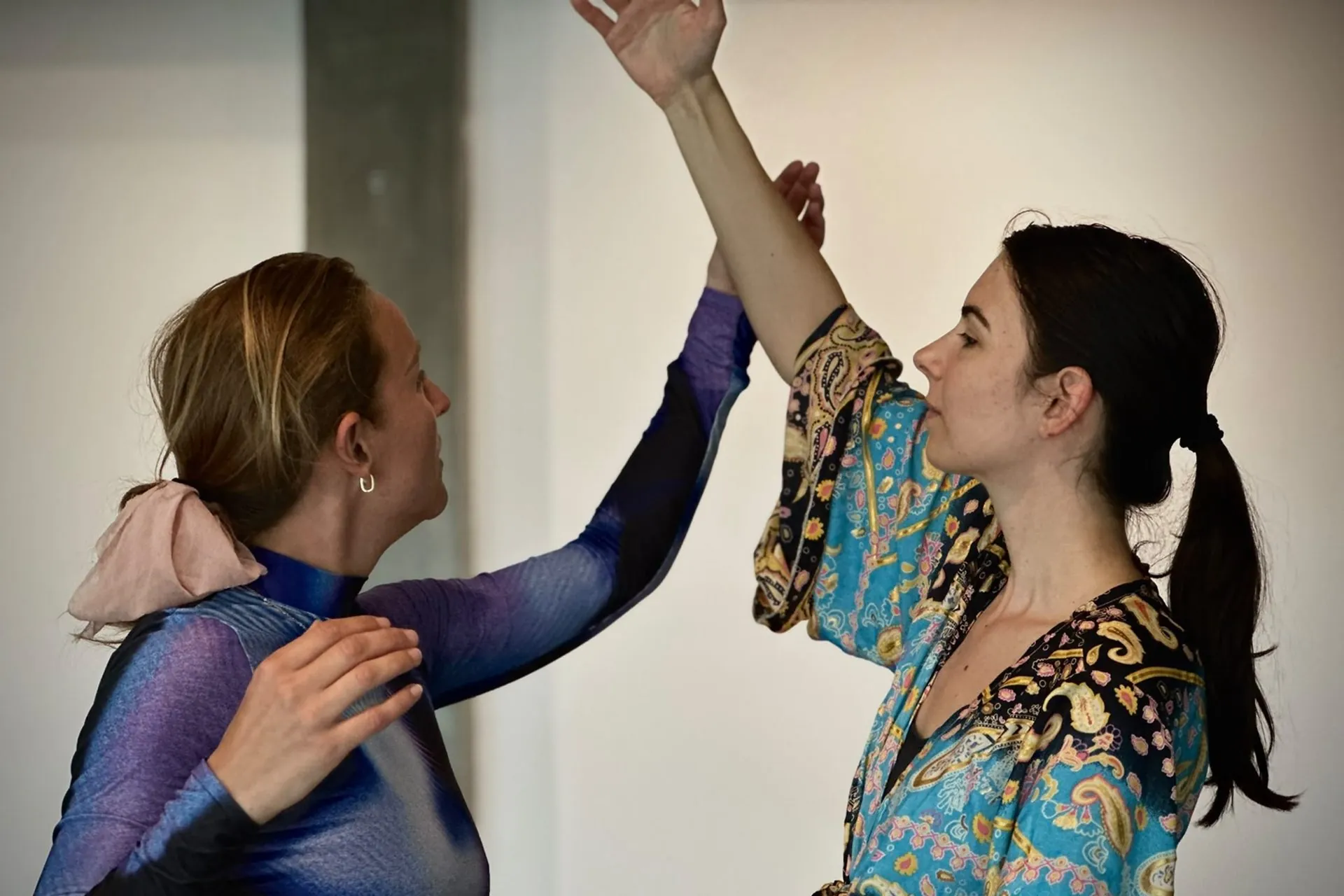 Twee vrouwen bewegen tegenover elkaar in een lichte zaal, elk met een opgeheven arm