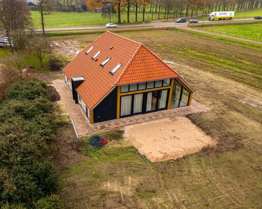 Een nieuwe woning met een oranje pannendak en donkere houten gevels, op een pas ingezaaid erf