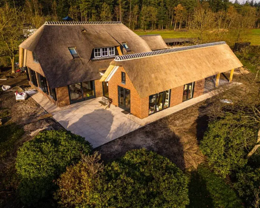 Een bakstenen woning met rieten kap en een lange aanbouw, van boven
