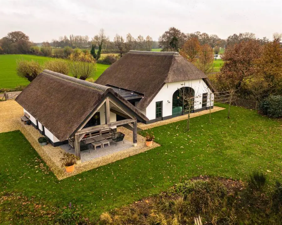 Een witte boerderij met rieten kap en een overkapping aan de achterkant