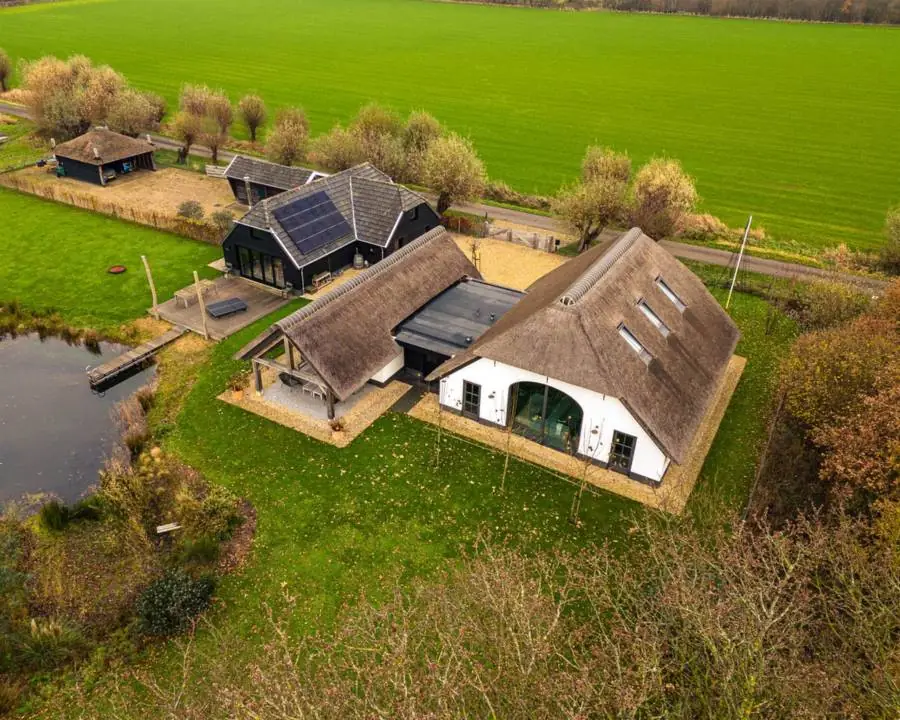 Een erf met een witte boerderij, bijgebouwen met rieten kap en een vijver, van hoog boven