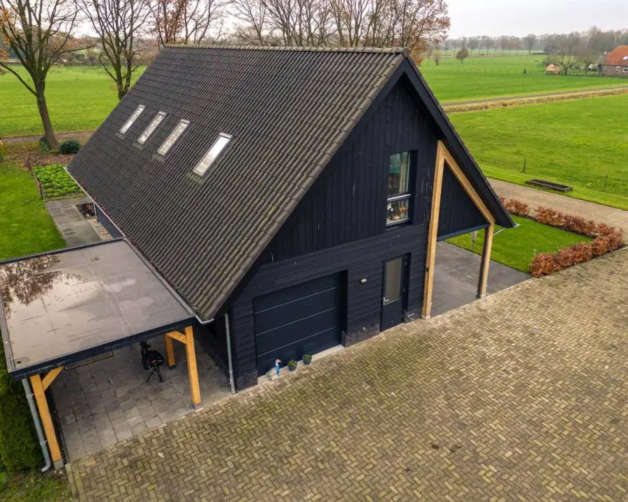 Een woning met zwarte houten gevels, dakramen en een carport van hout