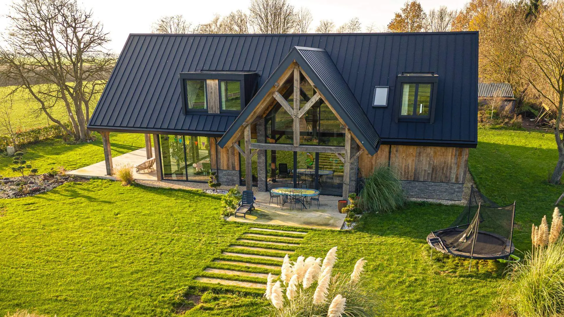 Werk van Bouwbedrijf Groters van boven: een woning met een zwart dak en een puntgevel van glas en eiken spanten, in de late middagzon